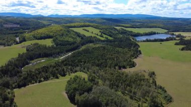 Göl, tarım arazileri, bir çiftlik ve bulutlu bir gökyüzünün altında yemyeşil bir kırsal bölgenin panoramik hava manzarası. Saint-Damase, Quebec, Kanada, 2025.