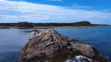 St. Lawrence Nehri 'nin dalgaları bulutlu bir gökyüzünün altında yemyeşil kıyıya yakın yükselen bir resifin kayalık kenarlarına nazikçe çarpar. Anse du Petit Mitis, Quebec, Kanada, 2025.