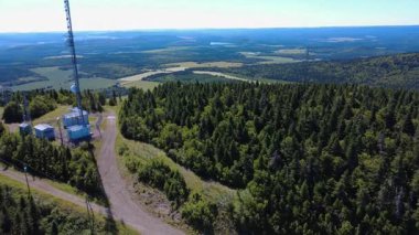 Toprak bir yolun yakınındaki telekomünikasyon kuleleri ve ekipmanlarla yuvarlanan dağların üzerindeki sık bir ormanın klibi, temiz bir gökyüzü altında geniş bir panoramik kırsal alan yakalıyor. Sainte-Irene, Quebec.