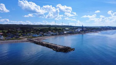 St. Lawrence nehri ve hendeğine yakın büyüleyici bir sahil köyü, eski bir balıkçı iskelesinin kalıntıları, evleri, kilisesi ve uzakta bir rüzgar çiftliği var. Baie-des-Sables, Quebec, Kanada, 2025.