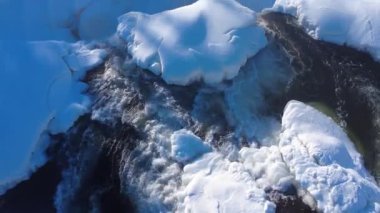 Buzlu bir şelalenin başındaki bir nehrin üzerinde alçaktan uçarak buzdaki karanlık bir boşluğa düşüyor..