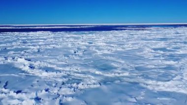 Uçsuz bucaksız donmuş deniz, berrak mavi gökyüzünün altında ufka doğru uzanır. Kırık buz kütleleri ve kar parçaları soğuk, izolasyon, dinginlik ve vahşi kutup doğasını taşır..