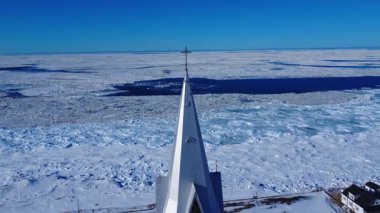 Üzerinde demirden bir haç bulunan bir kilise kulesi, açık mavi gökyüzünün altında ufka uzanan donmuş deniz ve buz sahalarına doğru uzanıyor. Baie-des-Sables, St Lawrence nehri, Quebec, Kanada.