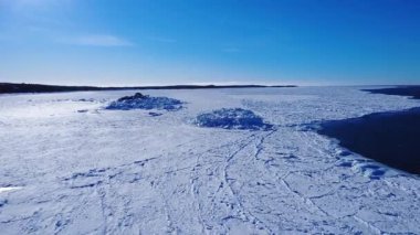 Donmuş bir okyanusun üzerinden kışın mavi gökyüzünün altında kıyı boyunca yükselen iki kayalık adaya bakan drone videosu. St. Lawrence Nehri, Metis-sur-Mer, Quebec, Kanada.