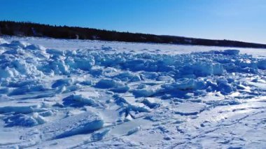 Uçsuz bucaksız, donmuş bir denizin yüzeyi. Kırık buz kütleleri ve karlı bir kıyı şeridi boyunca çatlaklarla kaplı. Mavi bir kış gökyüzünün altında. St. Lawrence Nehri, Gaspe Yarımadası, Quebec, Kanada.