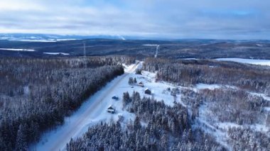 Karla kaplı kırsal bir yolun kış manzarası sık bir ormanın içinden geçiyor, kulübeler ve donmuş göllerle kaplı, dağlık bir alanda iletişim kulesi var. Sainte-Paule, Quebec, Kanada.