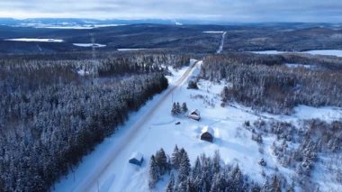 İki aracın panoramik hava görüntüsü kırsal bir yolda, karla kaplı ormanlı dağlarda, iletişim kulesinin yakınlarında seyahat ederken görülüyor. Sainte-Paule, Gasp Yarımadası, Quebec, Kanada.