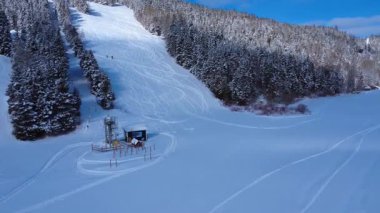 İki alp kayakçısı karla kaplı bir kayak pistine çıkarak, küçük, kapalı bir kayak kaldırma istasyonunun yakınında zikzak çizerek ilerliyorlar. Mont-Castor, Gasp Yarımadası, Quebec, Kanada. Kış 2026.
