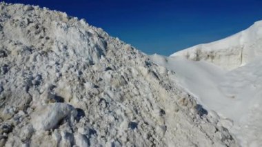 Geniş, donmuş deniz manzarası ön planda büyük kar tepecikleri, ufka uzanan düz buz sahaları ve soğuk, sakin, yalnızlık ve engin açıklık taşıyan açık mavi bir kış gökyüzü..