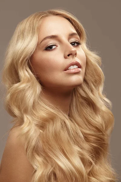 Blonde caucasian woman has long hair, beauty portrait of female face with natural skin on isolated light brown background.