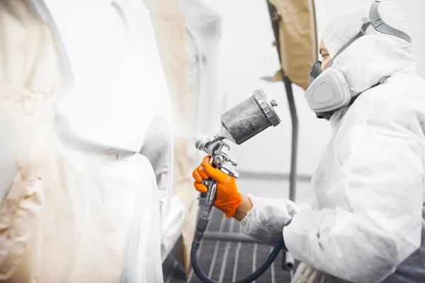 Pintor profesional de coches masculinos está pintando en el garaje por aerógrafo. Trabajador pinta vehículo con pistola de pulverización. — Foto de Stock