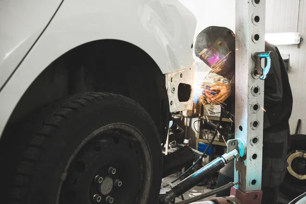 Industrial worker at car service welds automotive body. Metalworking with carbon dioxide welding.