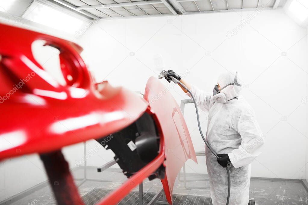 Car painter sprays varnish in paint booth.