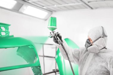 Koruyucu giysiler içinde ve araba tamponunu sprey boyayla boyayan bir erkek işçi..