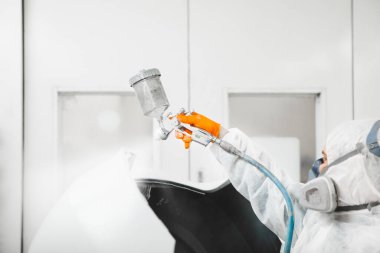 Araba boyacısı boya odasındaki araca beyaz boya püskürtüyor..