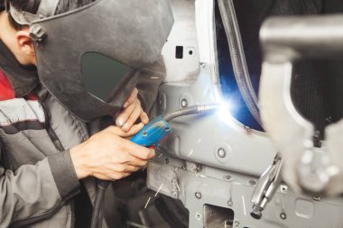 Koruyucu maskeli oto tamircisi araba kaynakçısı. Metal karbondioksit kaynaklarıyla çalışıyor. Endüstri ve kaporta tamiri kavramı.