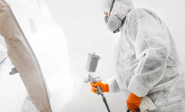 Trabajador masculino con máscara y ropa protectora pintando coche usando compresor de aerosol. —  Fotos de Stock