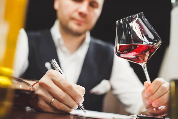 El hombre llena el formulario de papel sosteniendo delicioso vino tinto en la mesa — Foto de Stock
