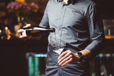 Adam yarı-karanlık restoranda şarap bardağına beyaz şarap döker.