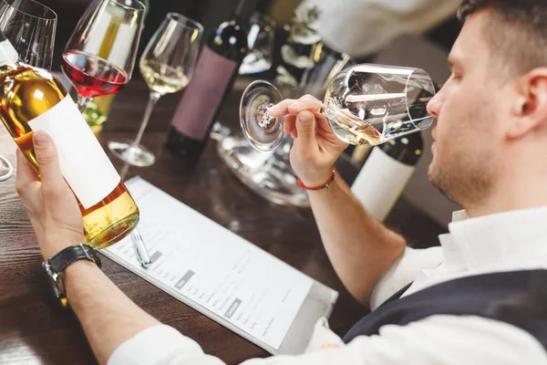 Vinho mordomo com forma cheira a bebida branca sentada à mesa — Fotografia de Stock
