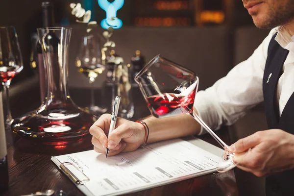 Especialista escreve segurando copo de vinho tinto caro na mesa Imagem De Stock