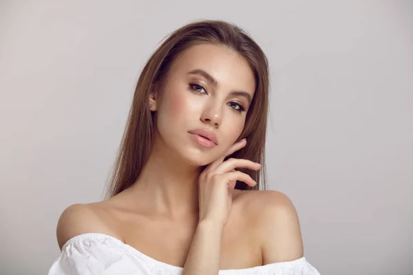 Pretty lady in white dress touches neck in light studio Royalty Free Stock Images