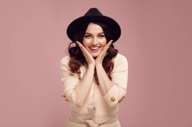 Şaşırmış bir ifadeyle dişlek, güler yüzlü, neşeli bir kadın ellerini pembe izole edilmiş bir şekilde yanaklarına koydu.