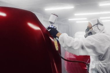 Odamdaki profesyonel araba boyacısı otomobil kaputu boyuyor. Adam kaputa boya püskürtüyor.. 