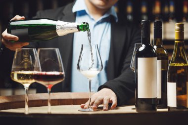 Meçhul şarap garsonu şarap mahzenindeki ahşap fıçının üzerine şişeden köpüklü şarap dolduruyor..