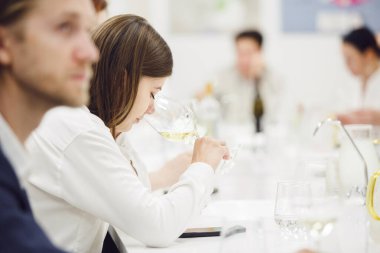 Profesyonel kadın şarap uzmanının beyaz şarap koklarken çekilmiş fotoğrafı. Camın rengini, tadını ve asit seviyesini analiz ediyor. Profesyonel şarap garsonu şarapla ilgili çeşitli dersler üzerinde çalışıyor.