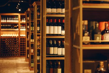 Modern şarap mahzeni çeşitli şarap şişeleriyle doluydu, yakın çekim fotoğrafçılığı. Ahşap raflarla dolu uzun koridor içki dükkanının mahzeninde seçkin şarap şişeleriyle doluydu. Restoranda ahşapla mahzen.