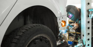 Koruyucu maskeli genç bir adam garajda eski bir arabayı tamir ediyor. Araç kaynağı. Karbondioksit kaynaklama.