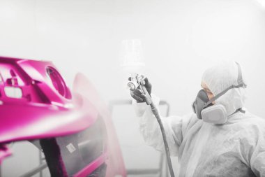 Coating of car body elements with paints and varnishes. Worker in a painting booth working with spray gun.