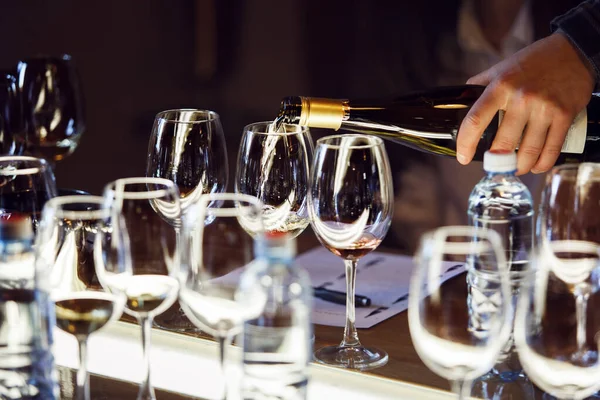 Masaya düzgünce yerleştirilmiş ince bardaklara beyaz şarap döken ve sofistike şarap tatma seanslarına hazırlanan kişinin fotoğrafını çek. Şarabı hazırlayın.