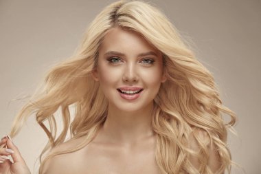 Bej izole arka planda uzun dalgalı saçlı güzel bir kızın güzel kadın portresi. Kafkasyalı genç bayanın gür bir saç stili var, kendine bir bak ve çekici bir gülümseme..