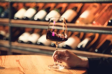 Kırmızı şarapla dolu bir şarap kadehi, bir mahzendeki ahşap bir masada nazikçe tutulur..