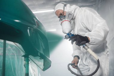 Araba boyacısı, araç atölyesinde sprey tabanca kullanarak araba gövdesine yeşil boya sıkıyor. Otomobil gövdesinin karmaşık restorasyonu, tam seçim rengi. 