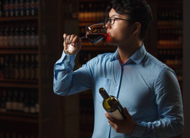 Profesyonel şarap tadımı yapan şarap mahzeninde ahşap fıçılar ve şişelerle çevrili şarap kadehlerini koklamak için yüzlerine tutuyorlar.