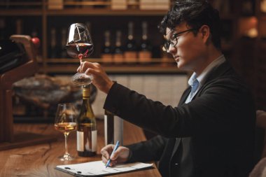Yetenekli erkek şarap garsonu şarap mahzeninde kırmızı şarap tadıyor, yakın çekim fotoğrafı. Alkollü içecekler degulasyonu. Şarap yapma okulu, şarap garsonu sertifikası. Profesyonel şarapçılar birliği.