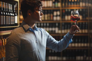 Şarap dükkanında duran yetenekli şarap garsonu elinde bir kadeh şarap, bir yudum almadan önce renkleri ve şarap aromasını inceliyor..