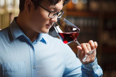 Profesyonel Asyalı şarap garsonu elinde tuttuğu cam parçalarını koklayarak kırmızı şarap aromasını incelikle değerlendiriyor.. 