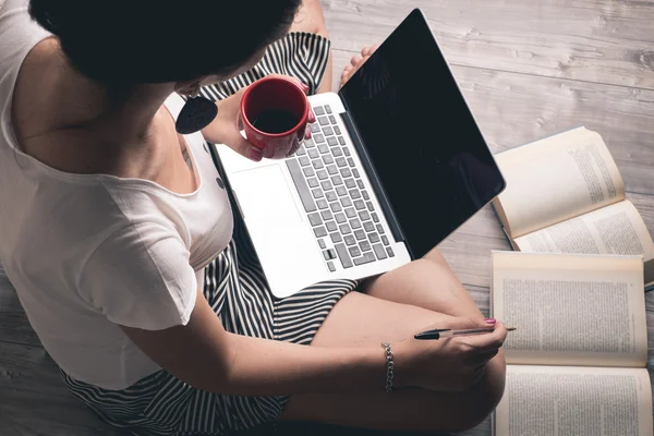 Menina olhando para um laptop com uma xícara de café — Fotografia de Stock