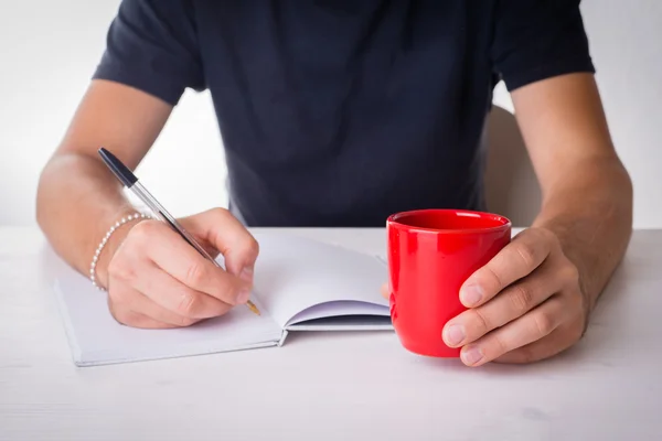 Mãos masculinas escrevendo com uma caneca e livros — Fotografia de Stock