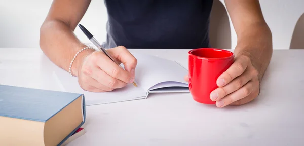 Mãos masculinas escrevendo com uma caneca e livros — Fotografia de Stock