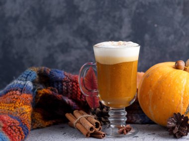 Masanın üzerinde renkli bir eşarp, tarçın ve sonbahar yapraklarıyla bir bardak balkabağı lattesi.