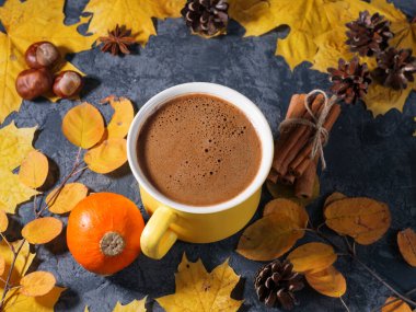 Masanın üzerinde sarı büyük bir fincan kahve renkli, parlak sonbahar yaprakları ve tarçınlı.