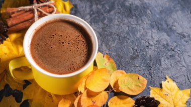 Masanın üzerinde sarı büyük bir fincan kahve renkli, parlak sonbahar yaprakları ve tarçınlı.