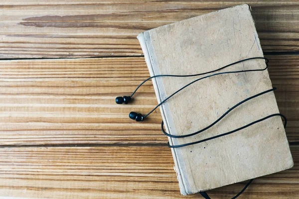 The concept of audio books. old book and headphones on wooden background with copy space