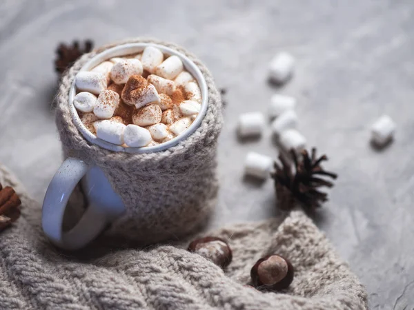 Hot winter drink chocolate, cocoa or coffee with marshmallows on the table in a knitted mug with cinnamon