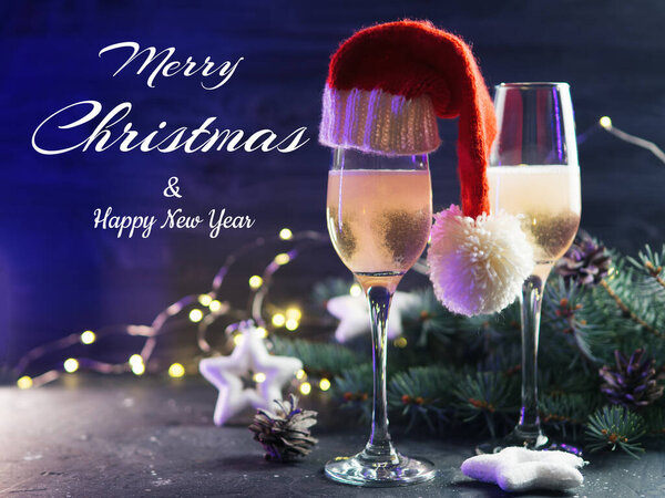 Merry Christmas greetings, two glasses of champagne in a Santa hat, tree branches and a garland
